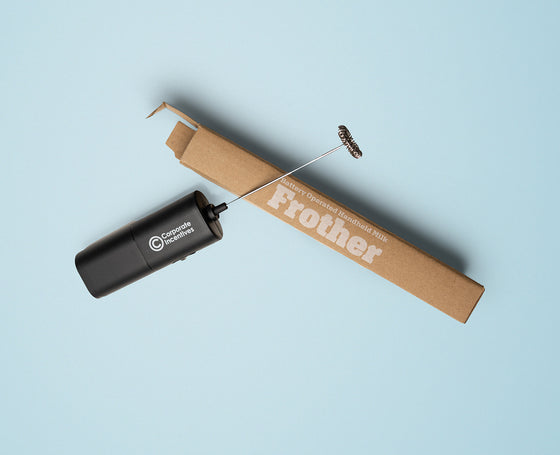 Black handheld frother with cardboard box on a light blue background