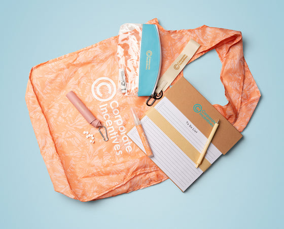 Collection of items including a pink tool, a blue item, a white card, and a brown folder on an orange cloth with 'Corporate Incentives' branding.