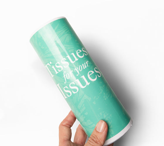 Turquoise cylindrical container with 'Tissues for your Issues' text held by a hand on a white background